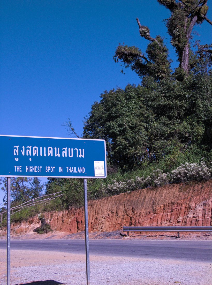 sign marking the highest point in Thailand, with a hill and obviously higher point behind it photographed by luxagraf