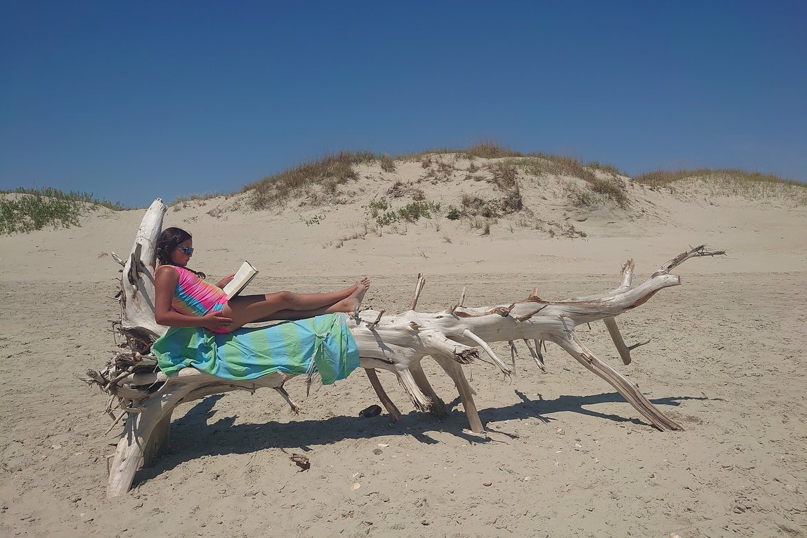 child lying on driftwood reading a book, ocracoke island, NC photographed by luxagraf