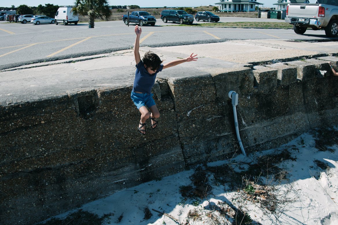 boy jumping off the seawall into the sand. photographed by luxagraf