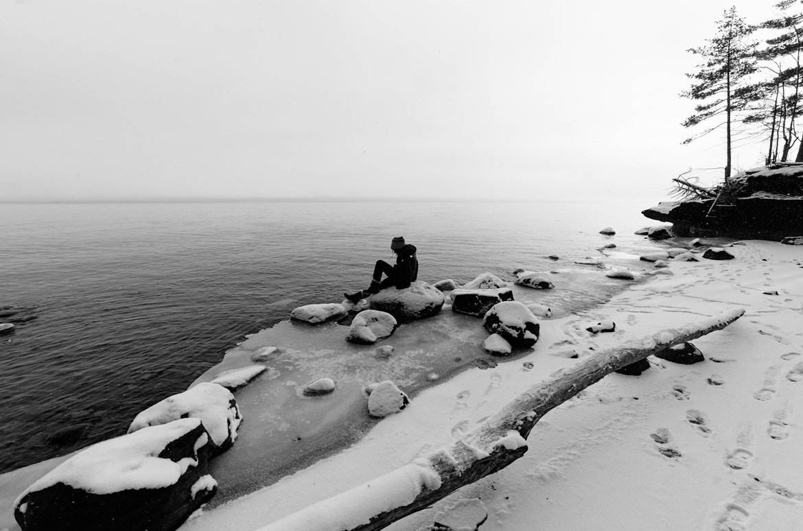 black and white image of girl on a rock snowy lakeshore photographed by Scott Gilbertson